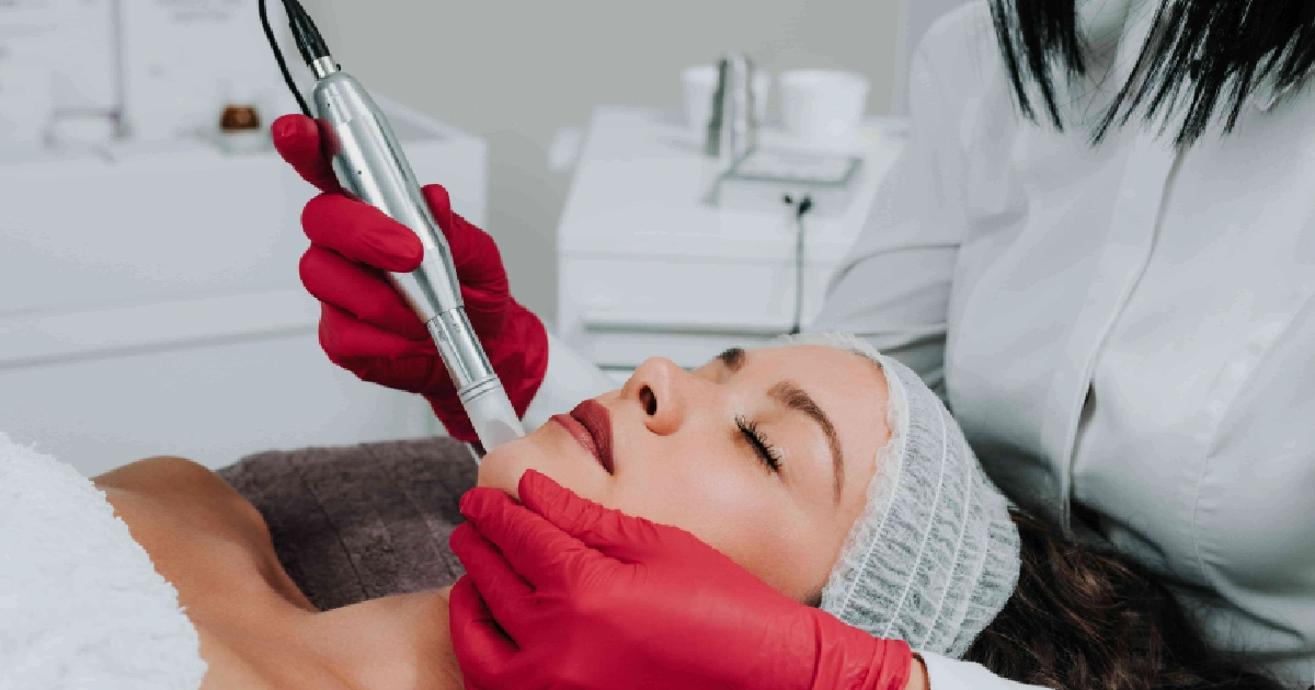 A woman in a white hair cap receives a Microneedling treatment in Reno, NV, on her chin, performed by a gloved professional with a small metallic tool.